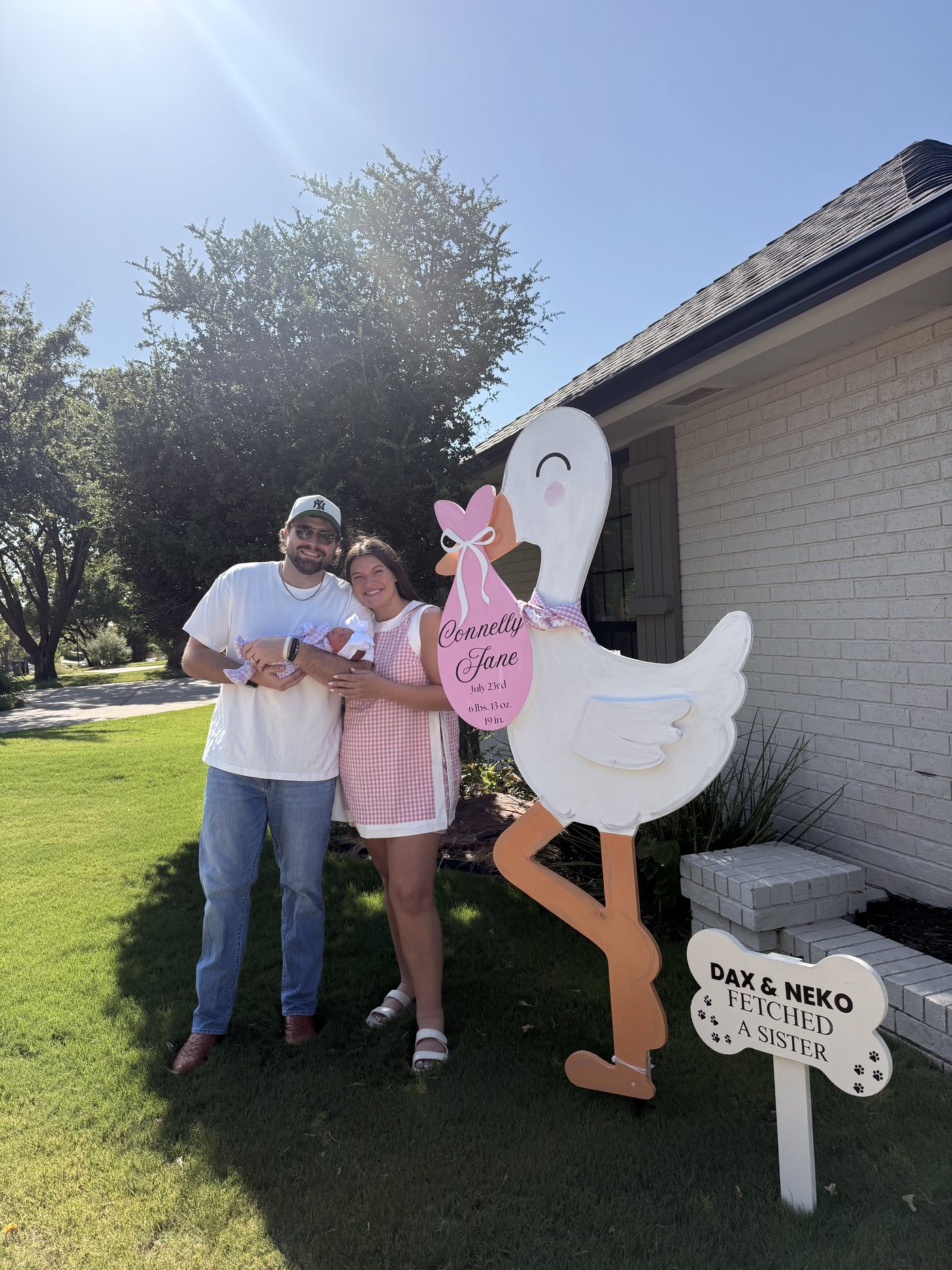 New parents holding their newborn beside a personalized stork yard sign in an Oklahoma City front yard